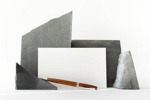 Abstract mockup template composition with white paper card, orange metallic parker pen and stones on white background.