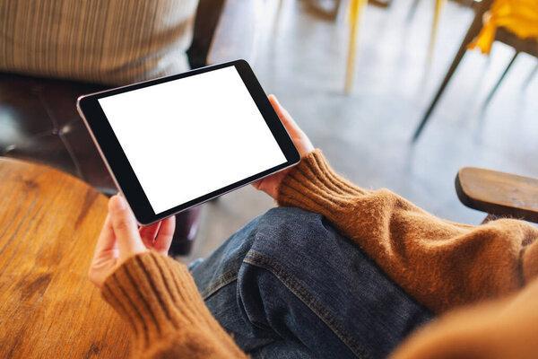 Mockup image of a woman sitting and holding black tablet pc with blank white desktop screen 