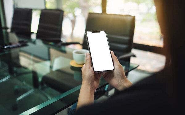 Mockup image of a woman holding mobile phone with blank white screen in office