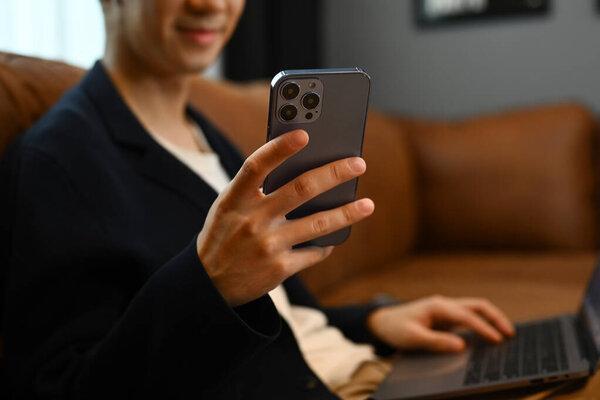 Young man sitting on couch with laptop, chatting with friends in social media via smartphone.