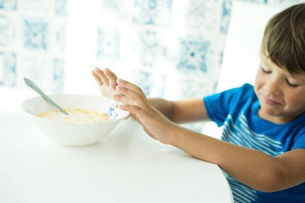 a boy in a blue T-shirt has breakfast with oatmeal and milk in a white plate, space for text, poor appetite, the child does not eat