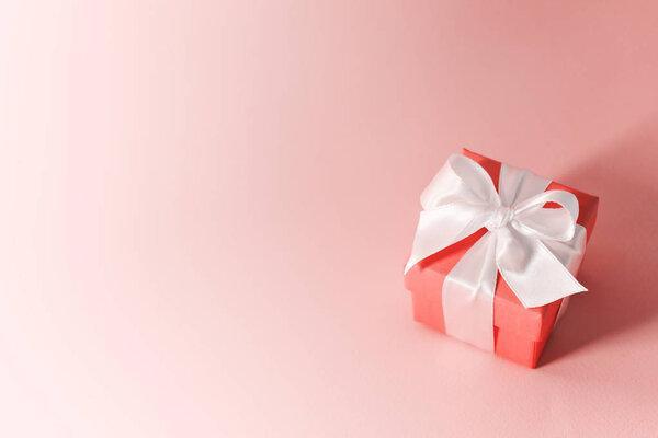 Close view of box tied with silk ribbon on living coral color pastel background