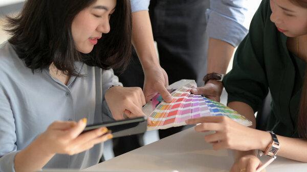 Close up view of young professional designer team consulting on their project with smartphone and coloured swatch in simple co working space