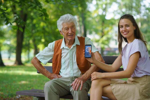 Caregiver helping senior diabetic man check his glucose data on smartphone. Diabetic senior using continuous glucose monitor. Granddaughter teaching her grandfather how to use smartphone, typing texts