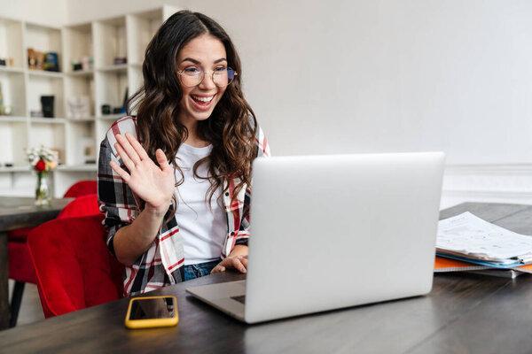 Cheerful nice woman waving hand and using laptop while sitting in cafe