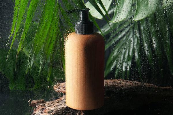 化妆品瓶和绿色在潮湿的玻璃杯后留下深色背景，特写
